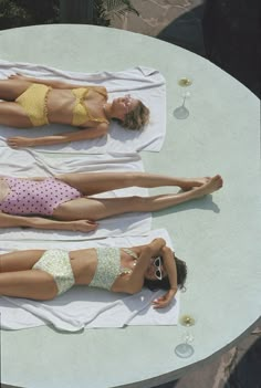 two women in bikinis are laying on towels at a table with wineglasses