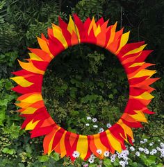 a large orange and yellow sunflower wreath in the middle of some bushes with white flowers around it