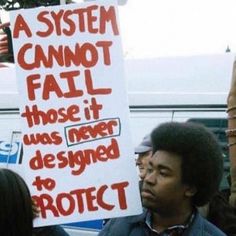 a man holding a sign that says a system cannot fail those it was never designed to protect