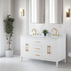 a white bathroom with two sinks and gold faucets on the counter top, along with a potted plant