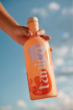 a person holding an orange bottle with the sky in the background and clouds behind it