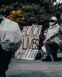 people sitting on the ground holding signs and umbrellas in front of them with black lives matter written on them