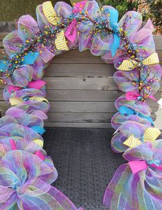 a purple and blue mesh wreath with bows on the front door, sitting next to a wooden fence