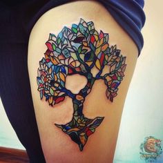 a woman's thigh with a colorful tree tattoo on it