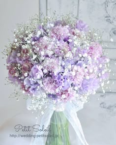 a bouquet of purple and white flowers in a glass vase with ribbon on the side