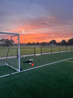 a soccer goal with the sun setting in the background and some balls on the ground