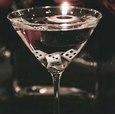 a martini glass with dice in it and a candle on the side that is lit