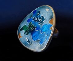 A gorgeous handcrafted enamel ring with primarily blue colors and other colorful accents. The ring has an engraved starburst pattern underneath the glass to give it a beautiful depth and texture.  Please feel free to ask me any additional questions you may have. Handmade Elegant Enamel Ring, Elegant Hand Painted Enamel Ring As A Gift, Elegant Hand Painted Enamel Ring Perfect For Gifting, Elegant Hand Painted Enamel Ring For Gift, Blue Oval Enamel Rings, Modern Enamel Ring For Gift, Unique Collectible Enamel Ring, Blue Oval Enamel Ring As Gift, Blue Oval Enamel Ring For Gift