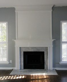 an empty living room with a fireplace and two windows in the corner, all painted white