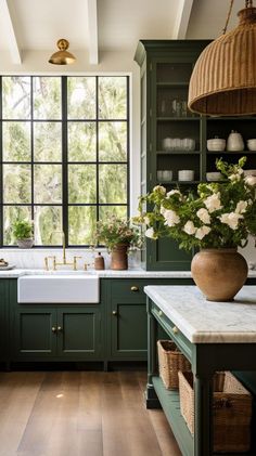 a kitchen with green cabinets and white flowers in a vase on the sink countertop