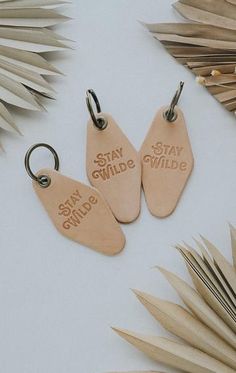 three leather keychains with the words stay wild on them next to palm leaves