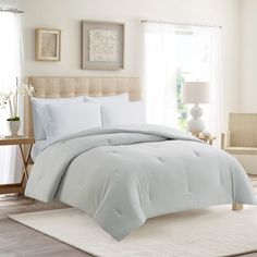 a bed with white comforters and pillows in a room next to a window,