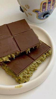 two pieces of chocolate on a plate next to a cup