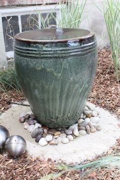 a large green planter sitting on top of a pile of rocks next to a metal ball