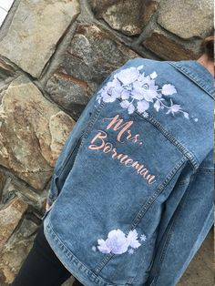 the back of a woman's jean jacket with embroidered flowers on it, next to a stone wall