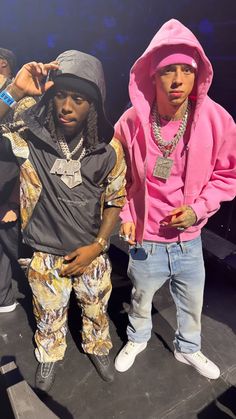 two young men standing next to each other in front of a stage with one wearing a pink hoodie