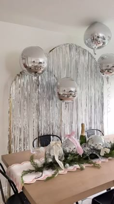 a dining room table is decorated with silver balloons and greenery for a festive look