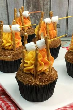 several cupcakes with marshmallows and candy sticks on them sitting on a white plate