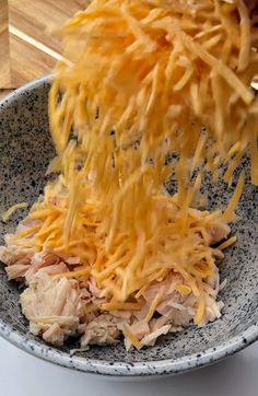 someone is sprinkling shredded cheese on top of chicken in a blue and white bowl