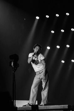 a man standing on top of a stage with his hands in his pockets while holding a microphone