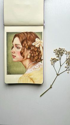 a small notepad with a drawing of a woman's face on it next to a flower