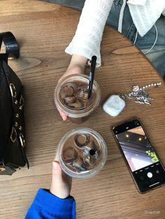 a person sitting at a table with some drinks and cell phone on the table next to them