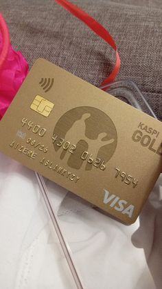 a gold visa card sitting on top of a white shirt next to a pink flower