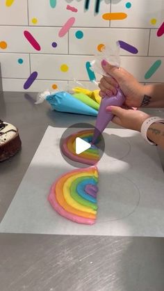 someone is decorating a rainbow cake with icing and sprinkles on the table