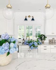 a kitchen with marble counter tops and blue flowers in a basket on the island top