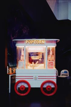 a small popcorn cart with red wheels and lights on the top, in front of a black background