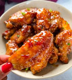 a person holding up a piece of chicken wings in a bowl with sauce on it