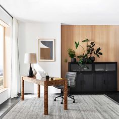 a living room with a desk, chair and plant in the corner next to a large window