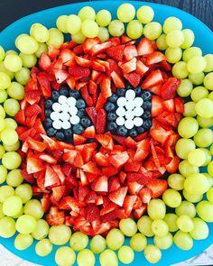 a blue plate topped with grapes and strawberries in the shape of a smiley face