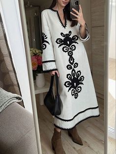 a woman taking a selfie while wearing a white and black dress with an embroidered design