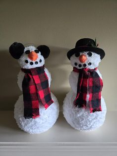 two snowmen with hats and scarves are sitting on a shelf, one is wearing a scarf