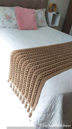 a crocheted blanket sitting on top of a bed next to pillows and blankets