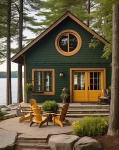 a green house with yellow doors and two chairs on the front porch next to trees