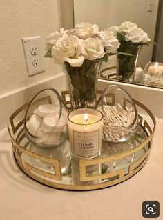 a candle and some flowers in a vase on a bathroom sink counter with two mirrors