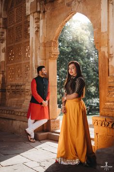 a man and woman standing next to each other in front of an archway with trees