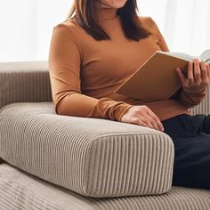 a woman sitting on a couch holding a book in her hands and smiling at the camera