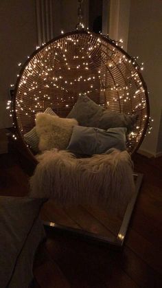 a hanging chair with lights on it in the middle of a living room, filled with pillows and blankets