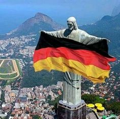 a flag flying in the wind next to a statue on top of a building with mountains in the background