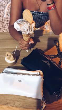 a woman eating an ice cream cone on top of a wooden table next to a purse