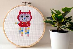 a potted plant sitting next to a cross - stitch cat