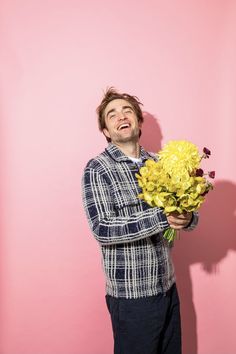 a man holding flowers in front of a pink wall