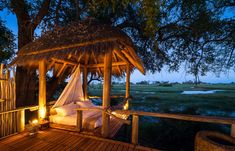 a bed in the middle of a wooden deck under a tree with lights on it