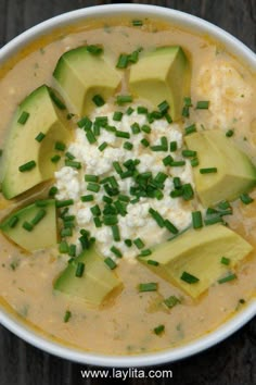 a white bowl filled with soup and topped with avocado slices, cottage cheese and chives