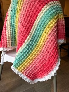 a multicolored crocheted blanket sitting on top of a white folding chair