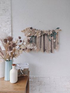 two vases with dried flowers on a table next to a white brick wall in a room