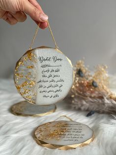 a person holding a white and gold ornament with writing on it in arabic